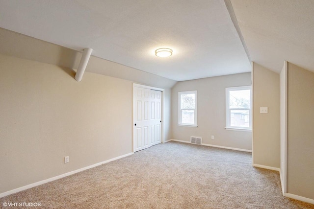 additional living space with light colored carpet, lofted ceiling, and a textured ceiling