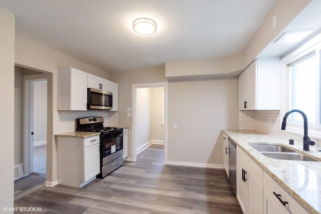 kitchen featuring white cabinets, sink, decorative backsplash, light stone countertops, and stainless steel appliances