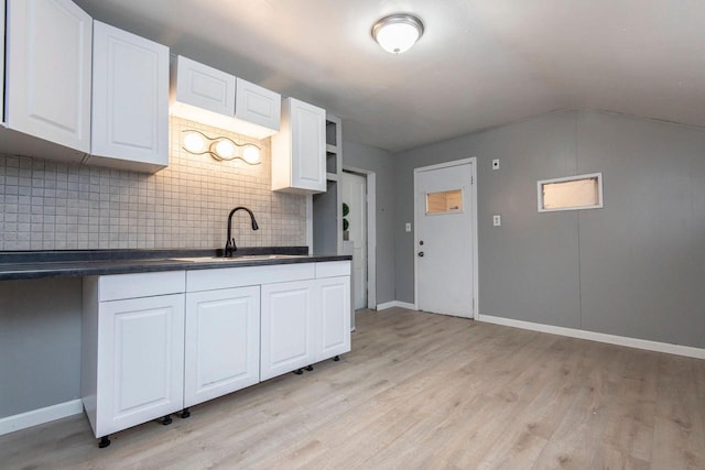 kitchen with decorative backsplash, white cabinetry, sink, and vaulted ceiling