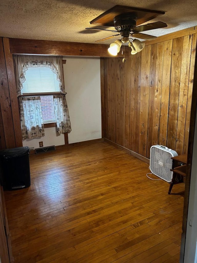 unfurnished room featuring wood walls, hardwood / wood-style floors, ceiling fan, and a textured ceiling