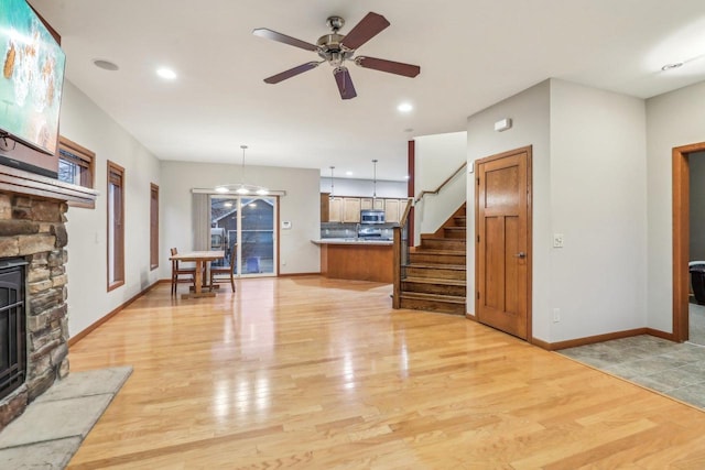 unfurnished living room featuring ceiling fan with notable chandelier, light wood-type flooring, and a fireplace