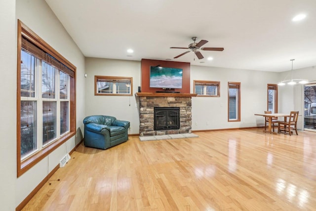 living room with light hardwood / wood-style flooring, a stone fireplace, and ceiling fan