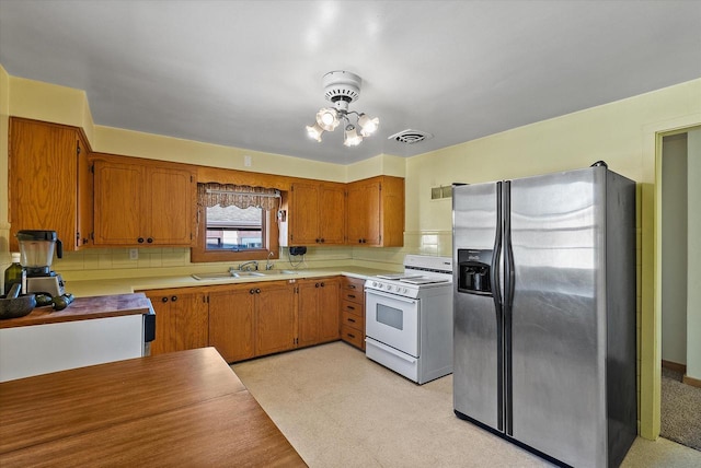 kitchen featuring sink, an inviting chandelier, stainless steel fridge with ice dispenser, backsplash, and white stove