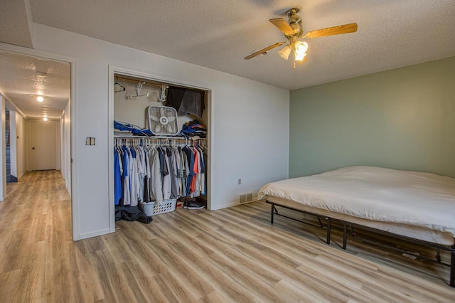 bedroom featuring a closet, a textured ceiling, light hardwood / wood-style floors, and ceiling fan