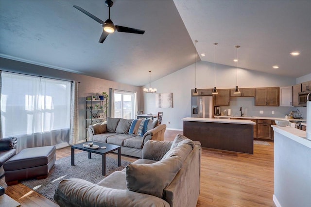 living room featuring ceiling fan with notable chandelier, light wood-type flooring, vaulted ceiling, and sink