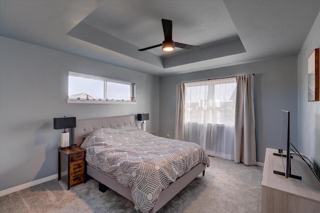 carpeted bedroom featuring a tray ceiling, multiple windows, and ceiling fan