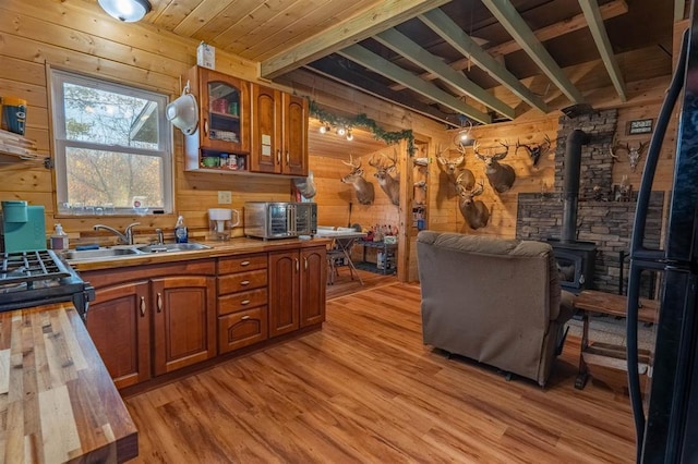 kitchen with a wood stove, wooden walls, sink, and light hardwood / wood-style floors