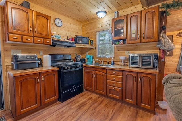 kitchen featuring sink, wooden ceiling, black gas range oven, and wooden walls