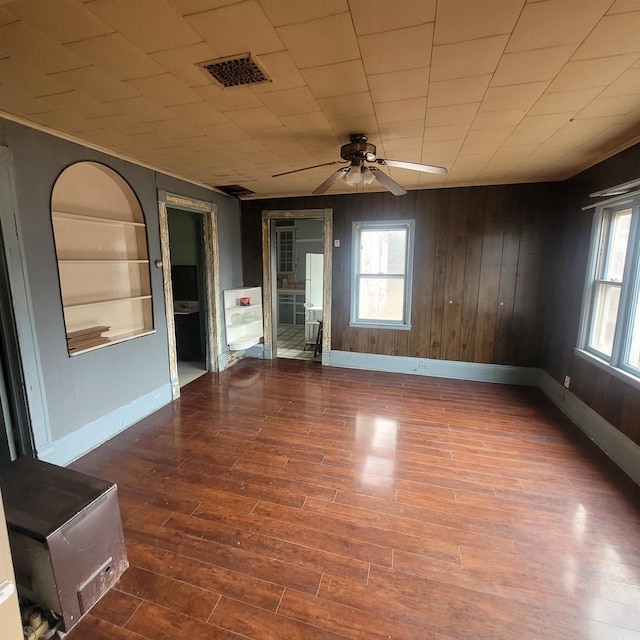 empty room featuring built in shelves, hardwood / wood-style flooring, ceiling fan, and wooden walls