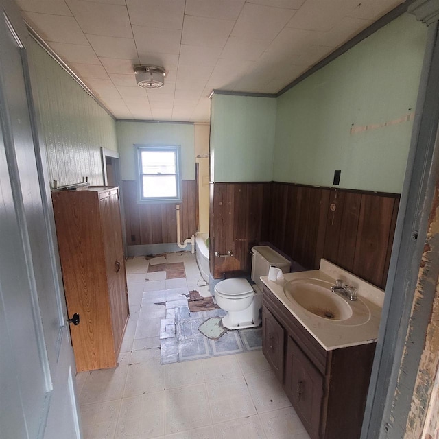 bathroom with wood walls, a washtub, vanity, and toilet