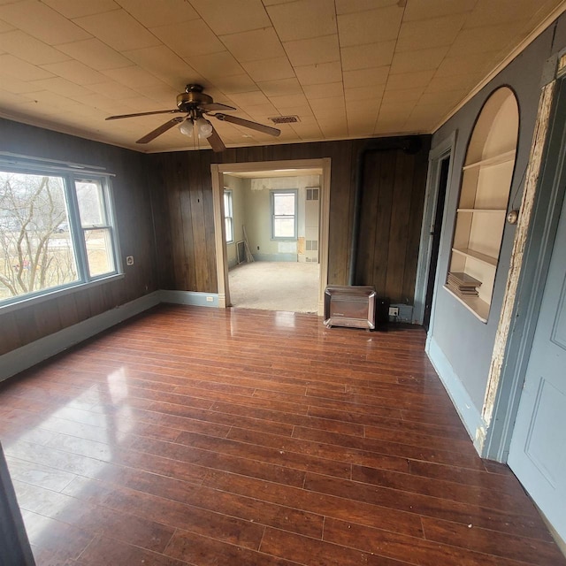 empty room with a wealth of natural light, ceiling fan, and wood walls