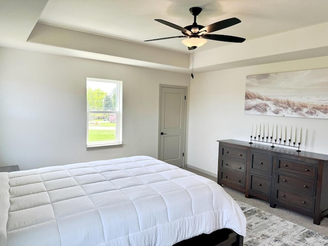 carpeted bedroom featuring ceiling fan and a tray ceiling