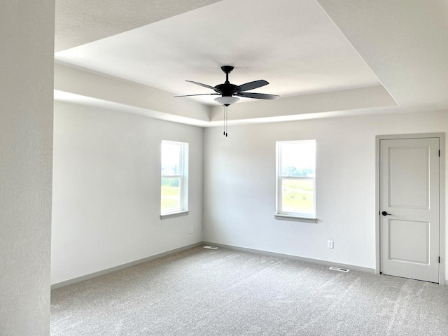 carpeted empty room featuring ceiling fan and a raised ceiling