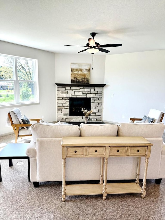 living room featuring carpet, a stone fireplace, and ceiling fan