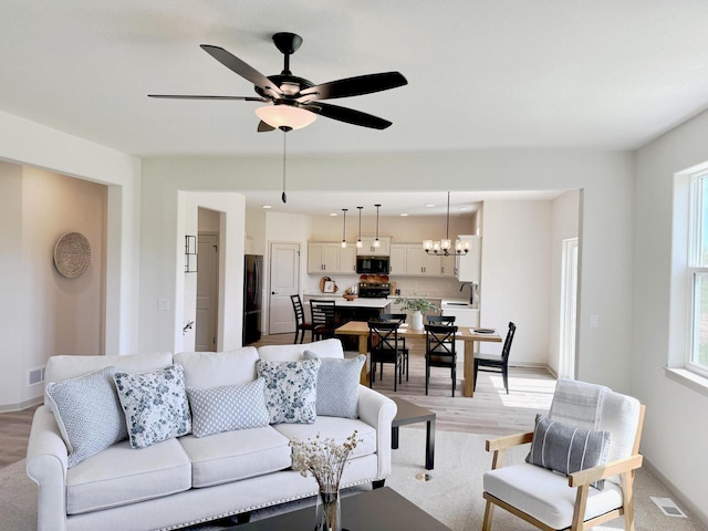 living room with light hardwood / wood-style flooring, ceiling fan with notable chandelier, and sink