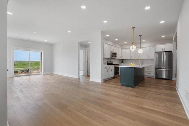 kitchen with white cabinets, hanging light fixtures, an island with sink, light hardwood / wood-style floors, and stainless steel appliances