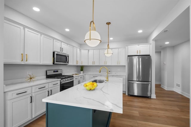 kitchen featuring white cabinets, hanging light fixtures, sink, an island with sink, and appliances with stainless steel finishes