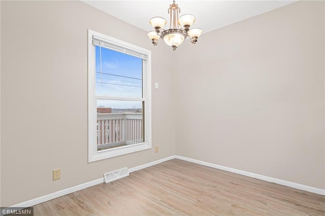 spare room with light hardwood / wood-style floors and a notable chandelier