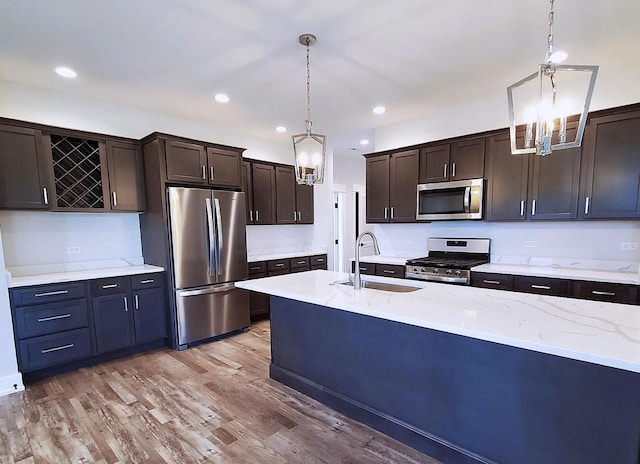 kitchen with appliances with stainless steel finishes, light wood-type flooring, dark brown cabinetry, sink, and pendant lighting