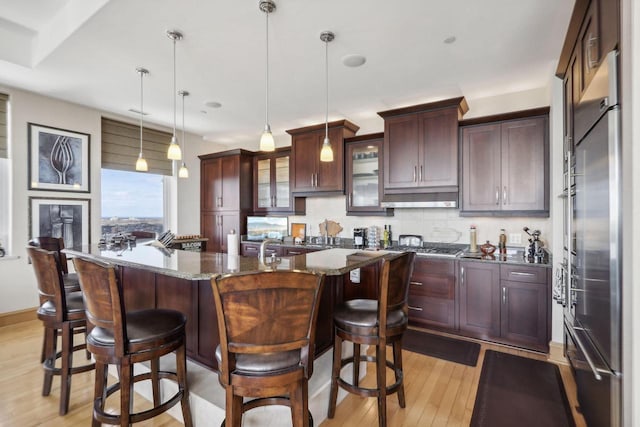 kitchen featuring a kitchen breakfast bar, backsplash, dark stone counters, a center island with sink, and hanging light fixtures