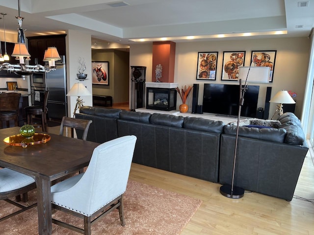 living room featuring light hardwood / wood-style floors, a raised ceiling, and a multi sided fireplace