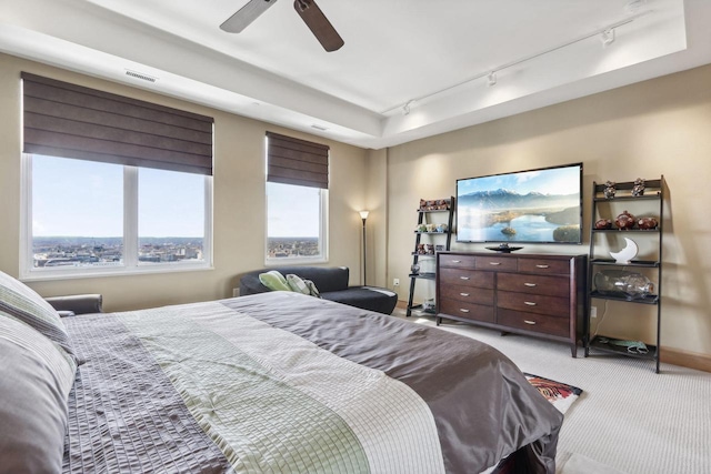 bedroom featuring light carpet, track lighting, ceiling fan, and a tray ceiling