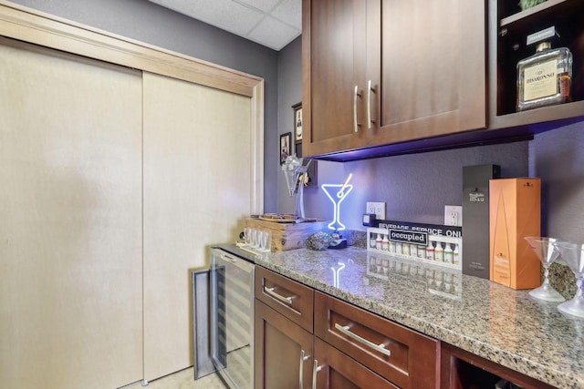 kitchen with wine cooler, light stone countertops, and a drop ceiling