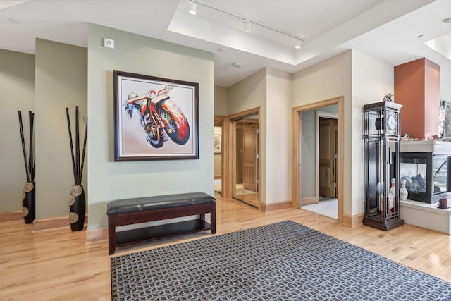 corridor with a tray ceiling, light hardwood / wood-style floors, and track lighting