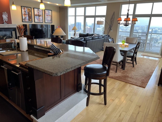 kitchen with light wood-type flooring, dark stone counters, sink, decorative light fixtures, and a chandelier