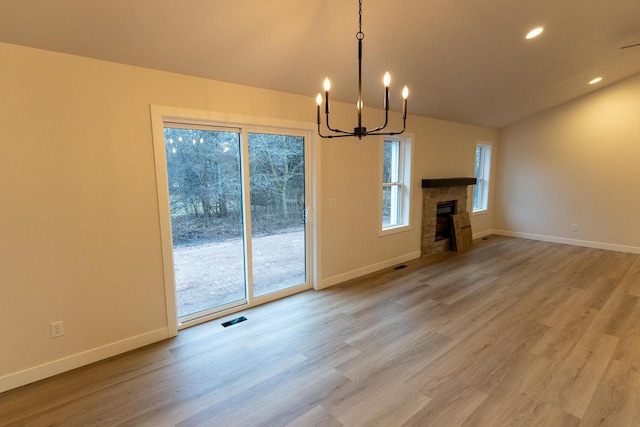 unfurnished living room featuring a tiled fireplace, an inviting chandelier, a healthy amount of sunlight, and hardwood / wood-style flooring