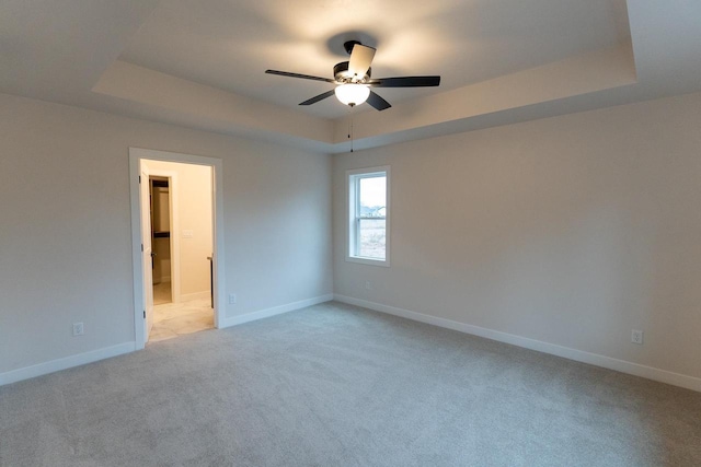 unfurnished room with a raised ceiling, light carpet, and ceiling fan