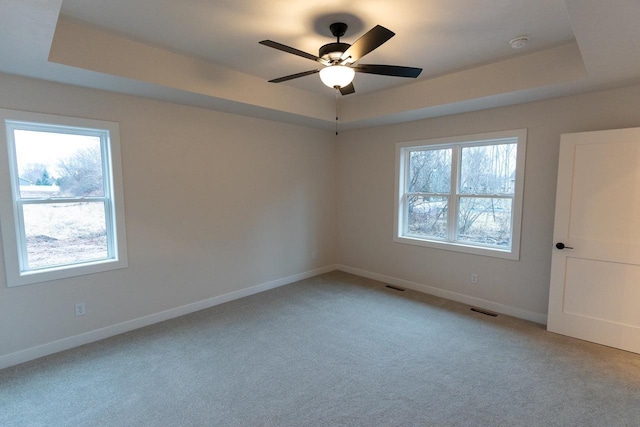 carpeted empty room with ceiling fan, a raised ceiling, and plenty of natural light