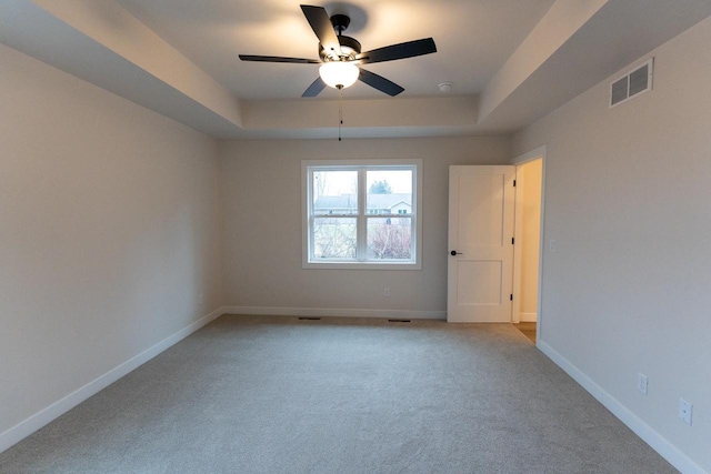 unfurnished room featuring ceiling fan, light colored carpet, and a tray ceiling