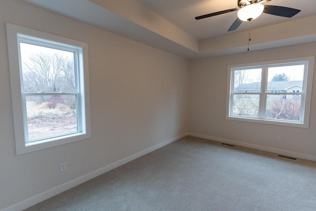 unfurnished room featuring ceiling fan, carpet floors, a wealth of natural light, and a tray ceiling