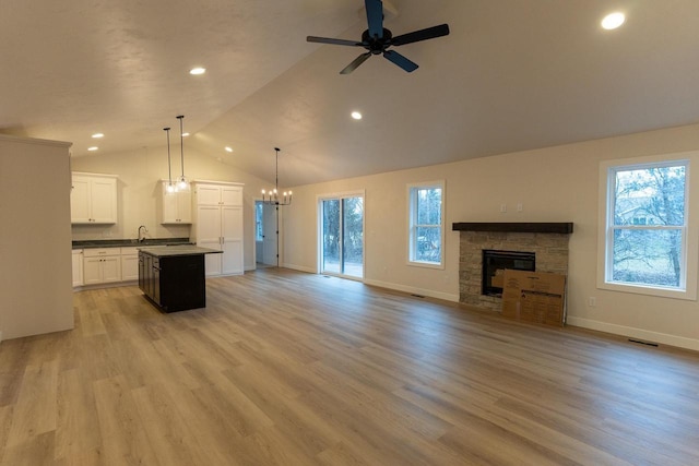 unfurnished living room featuring a fireplace, light wood-type flooring, and ceiling fan with notable chandelier