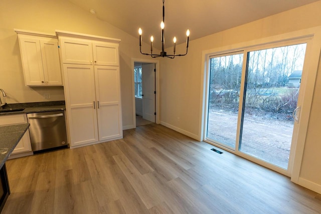 kitchen with stainless steel dishwasher, vaulted ceiling, sink, a notable chandelier, and white cabinetry