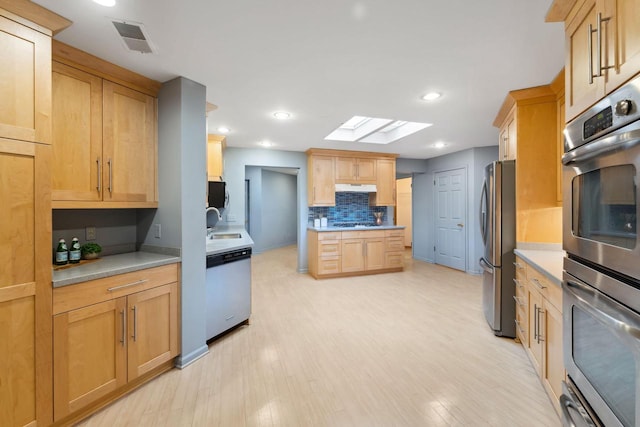 kitchen featuring sink, a skylight, decorative backsplash, light brown cabinetry, and stainless steel appliances