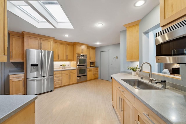 kitchen featuring sink, a skylight, light brown cabinetry, appliances with stainless steel finishes, and light hardwood / wood-style floors