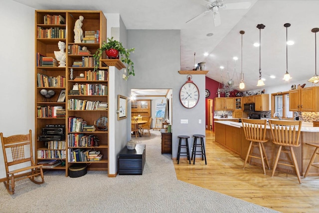 kitchen featuring lofted ceiling, a kitchen breakfast bar, ceiling fan, decorative light fixtures, and light hardwood / wood-style floors