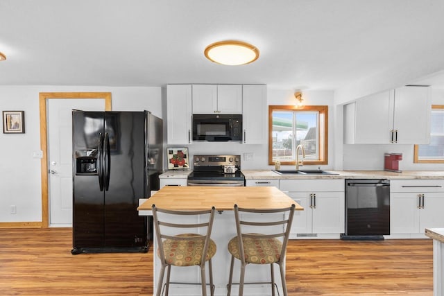 kitchen with white cabinets, sink, light hardwood / wood-style floors, and black appliances