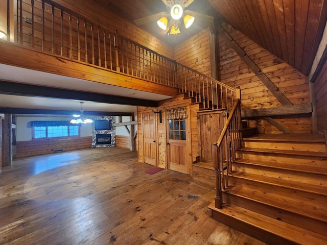 interior space with brick wall, ceiling fan with notable chandelier, hardwood / wood-style flooring, wooden ceiling, and a high ceiling