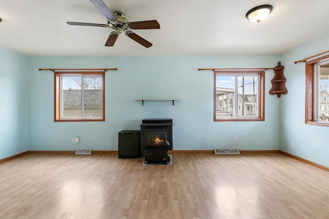 unfurnished living room with a wood stove, ceiling fan, light hardwood / wood-style flooring, and a healthy amount of sunlight