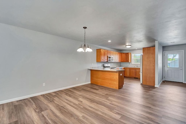 kitchen featuring kitchen peninsula, appliances with stainless steel finishes, light wood-type flooring, decorative light fixtures, and an inviting chandelier