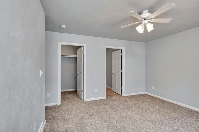 unfurnished bedroom featuring a closet, a walk in closet, light colored carpet, and ceiling fan