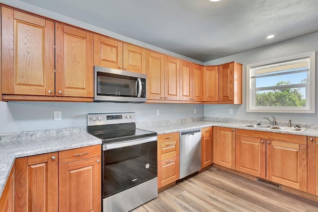 kitchen featuring stainless steel appliances, light stone counters, light hardwood / wood-style floors, and sink