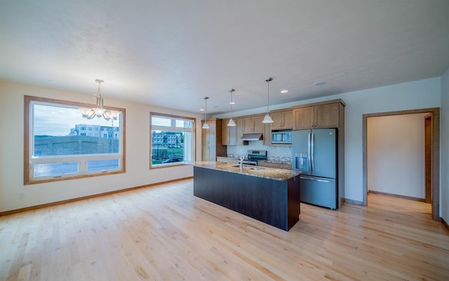 kitchen featuring hanging light fixtures, stainless steel appliances, a center island with sink, and light hardwood / wood-style flooring