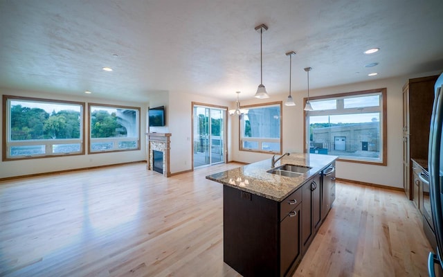 kitchen featuring sink, a fireplace, an island with sink, decorative light fixtures, and light stone counters