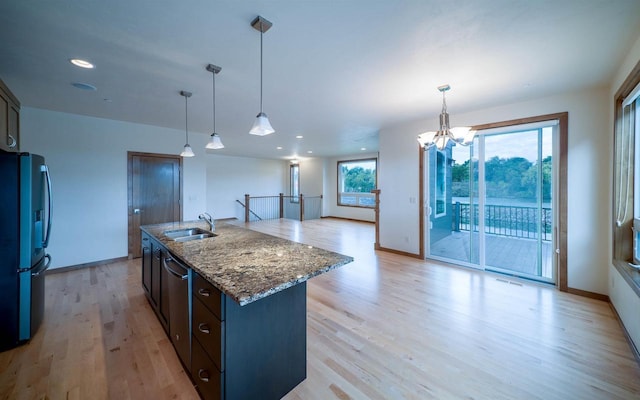 kitchen with stainless steel fridge, a center island with sink, decorative light fixtures, and sink