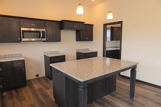 kitchen with a center island, dark hardwood / wood-style floors, light stone countertops, decorative light fixtures, and dark brown cabinetry