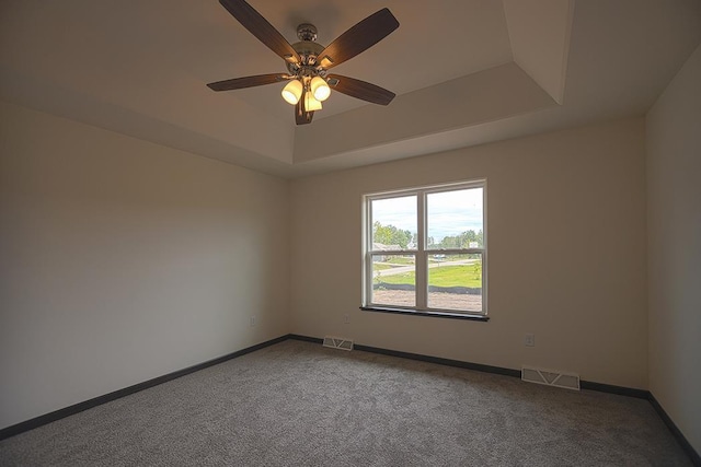 spare room featuring a raised ceiling, ceiling fan, and carpet flooring